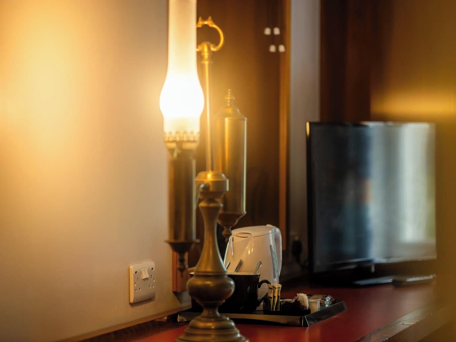 Ett hotellrum med en lampa, en kaffebryggare och en tv-apparat placerade på en träyta.