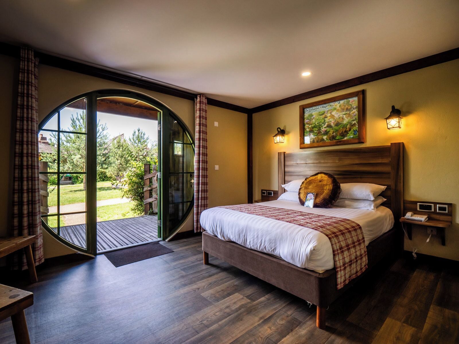 A bedroom with a large bed, a wooden headboard, a nightstand, a wall-mounted lamp, and a painting.