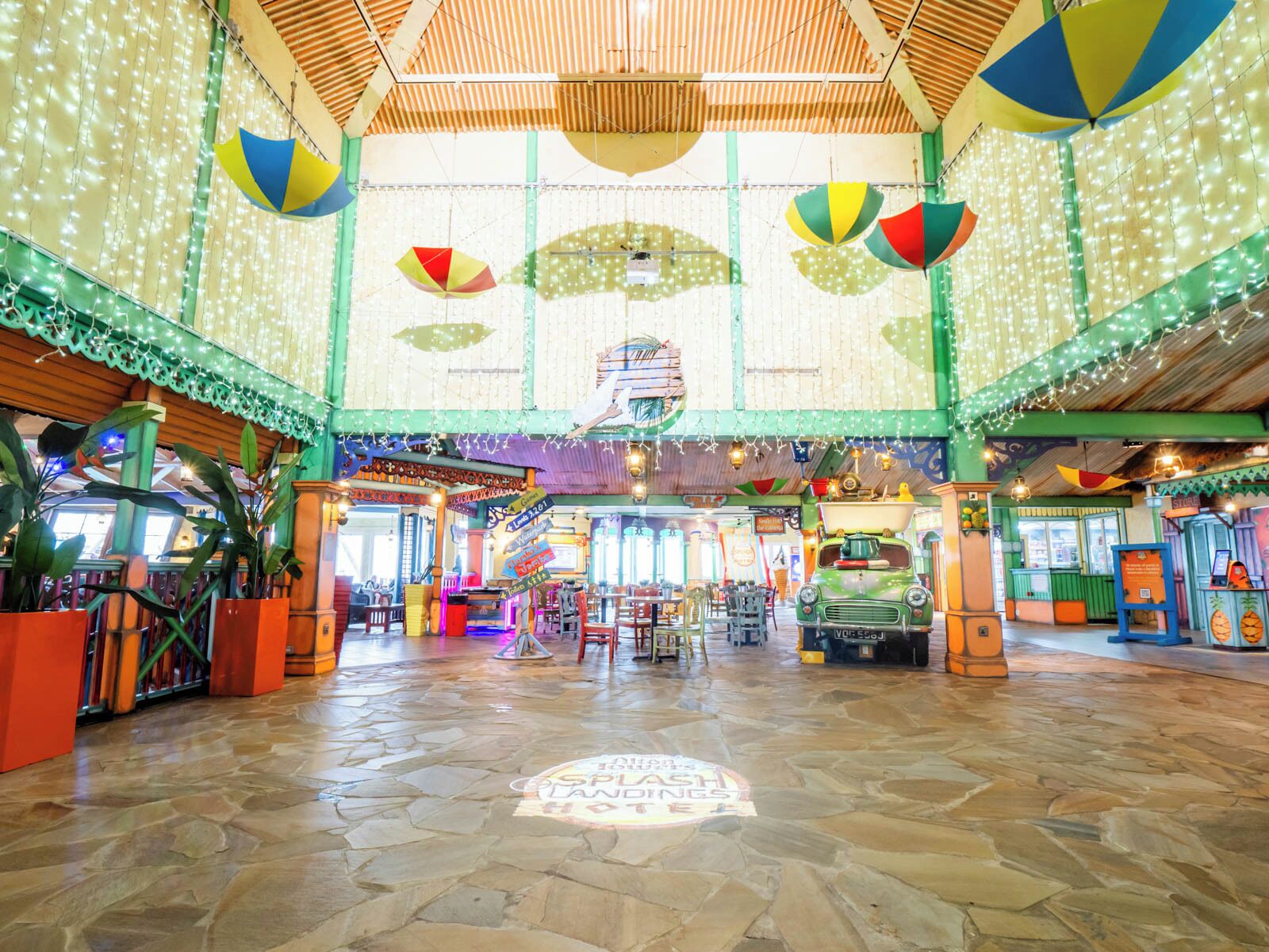 A spacious indoor area with a stone floor, colorful hanging decorations, and various booths and kiosks.