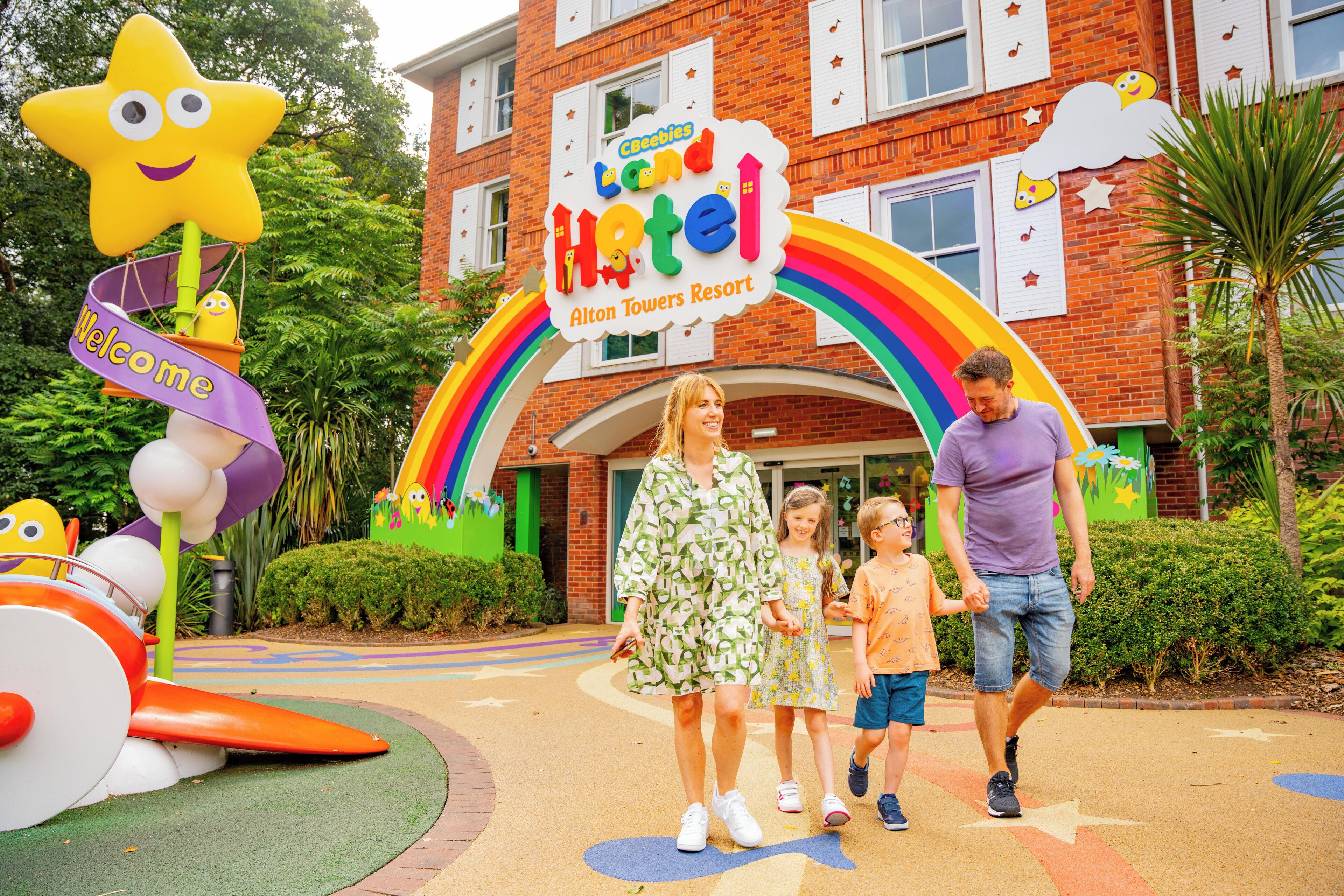 A family walking towards a hotel entrance with a colorful sign and playful decorations.