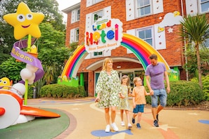 A family walking towards a hotel entrance with a colorful sign and playful decorations. - Alton Towers Hotel (Stoke-on-Trent)