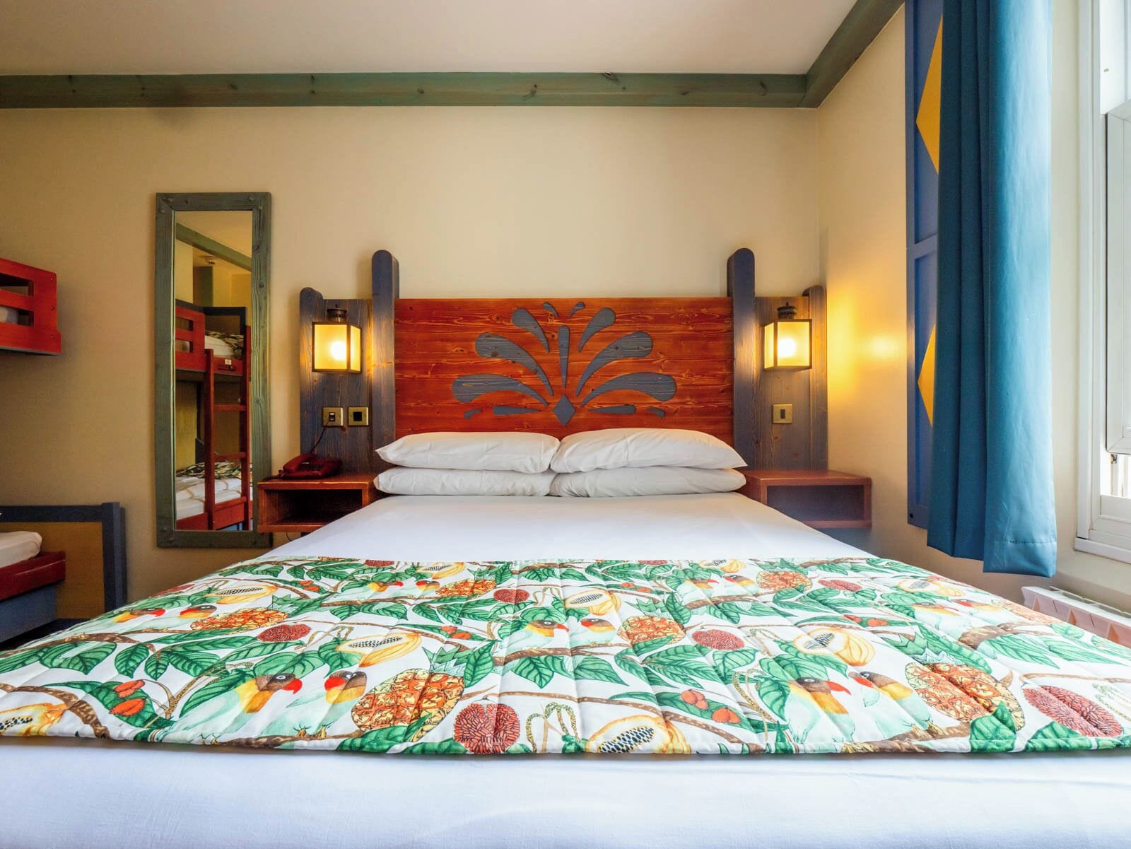 Habitación de hotel con una cama grande, cabecera de madera, dos lámparas de noche, mesita de noche y un espejo.