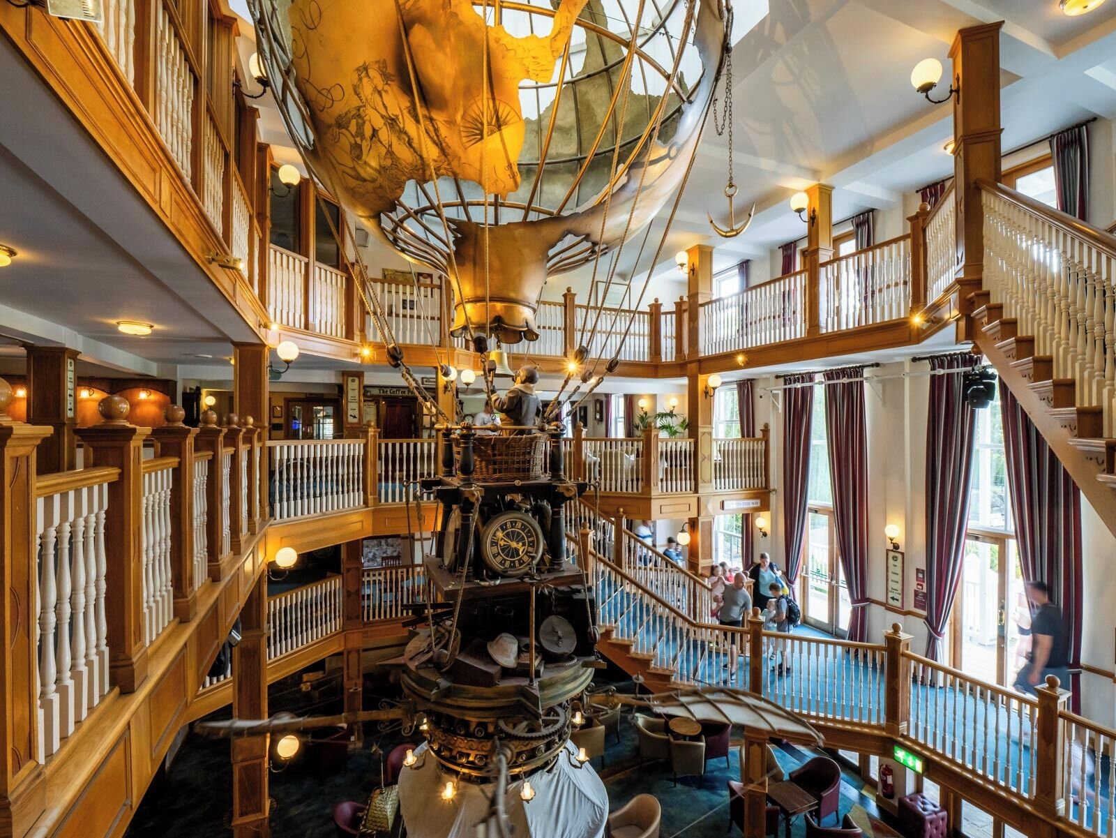 Un interior de varios niveles con barandas de madera, una estructura decorativa central que recuerda a un barco y una escalera.