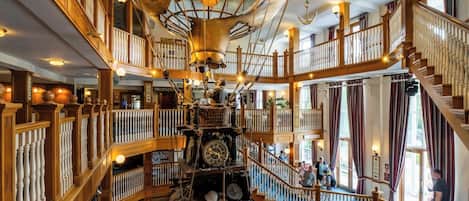 Un interior de varios niveles con barandas de madera, una estructura decorativa central que recuerda a un barco y una escalera.