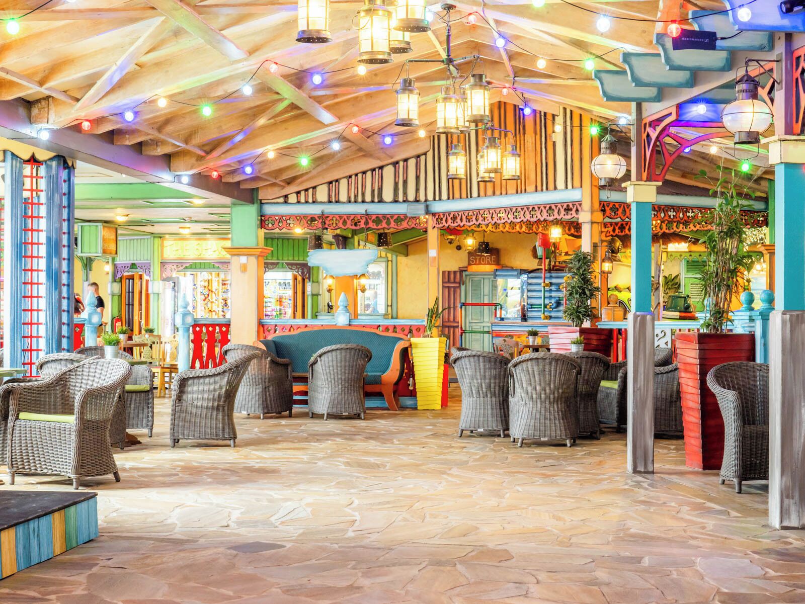 A spacious indoor area with wicker furniture, a stone floor, and a variety of hanging lights.