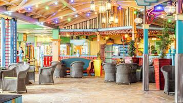 A spacious indoor area with wicker furniture, a stone floor, and a variety of hanging lights.