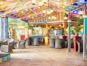 A spacious indoor area with wicker furniture, a stone floor, and a variety of hanging lights.