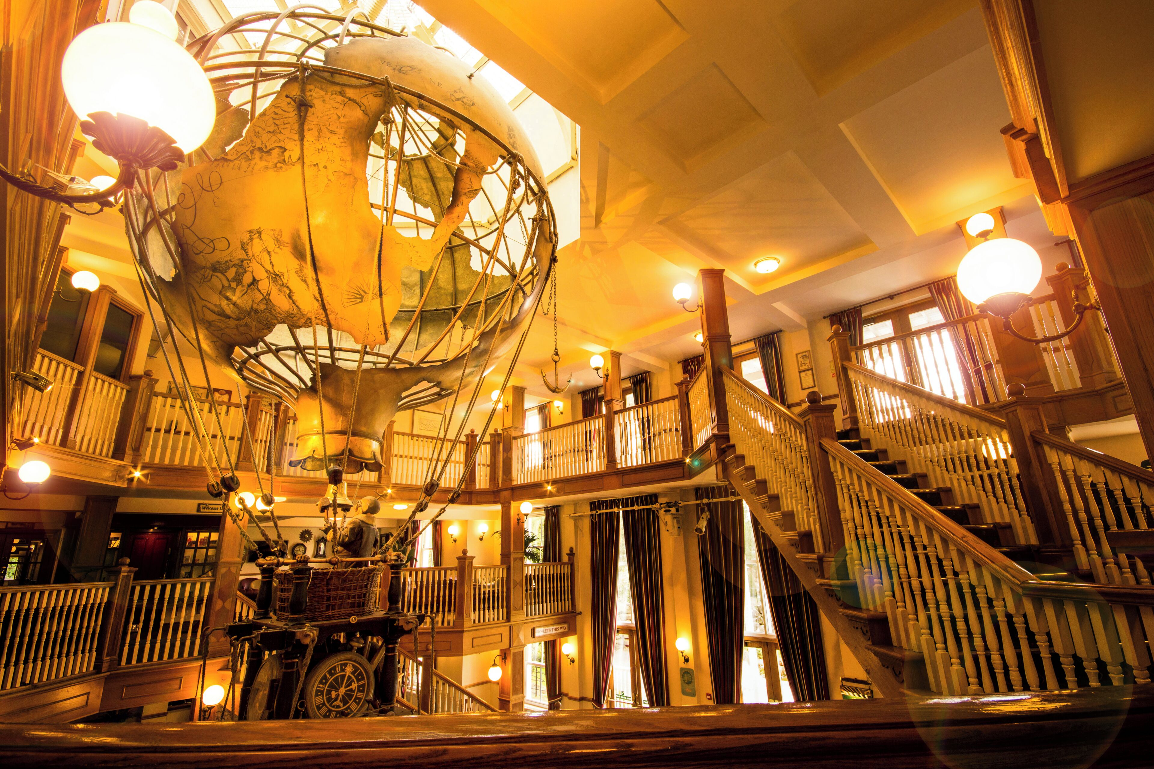 A grand interior with a large globe, wooden staircases, and a welcoming sign.