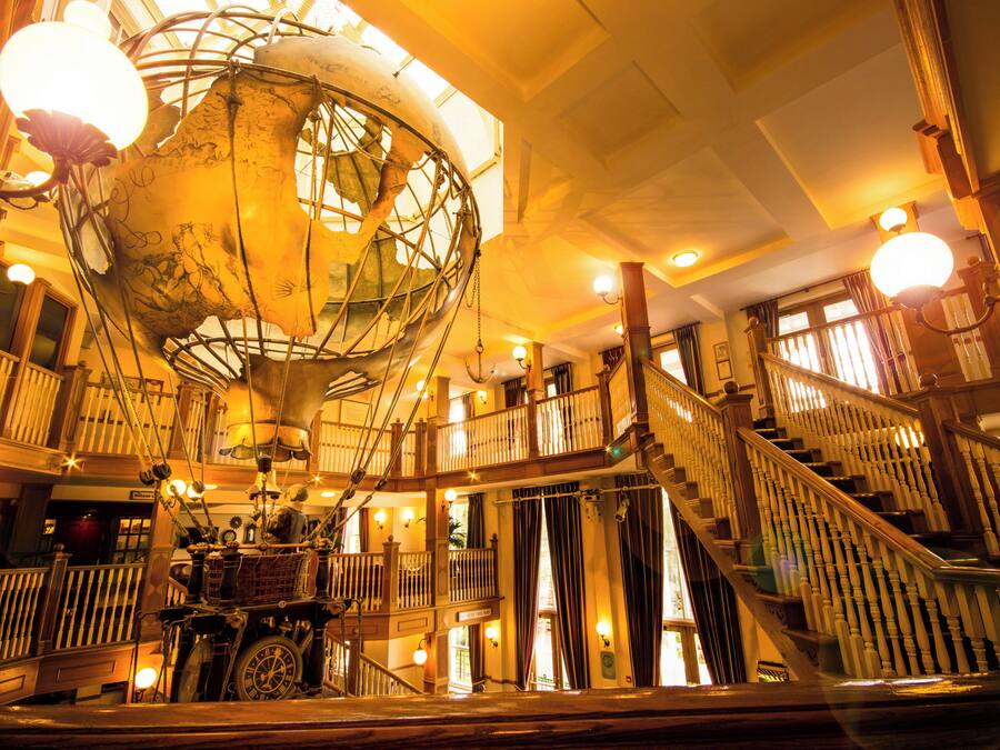 A grand interior with a large globe, wooden staircases, and a welcoming sign.