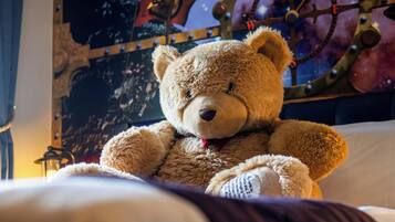 A plush teddy bear on a bed with a starry night backdrop and a ship's wheel.
