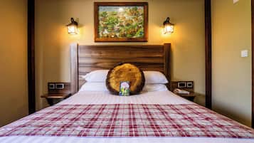Habitación de hotel con una cama grande, dos lámparas de noche, un cuadro en la pared y una colcha a cuadros.