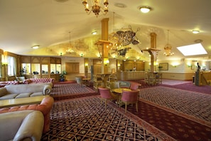 Um amplo hall de hotel com teto alto, lustres elaborados e um bar central.