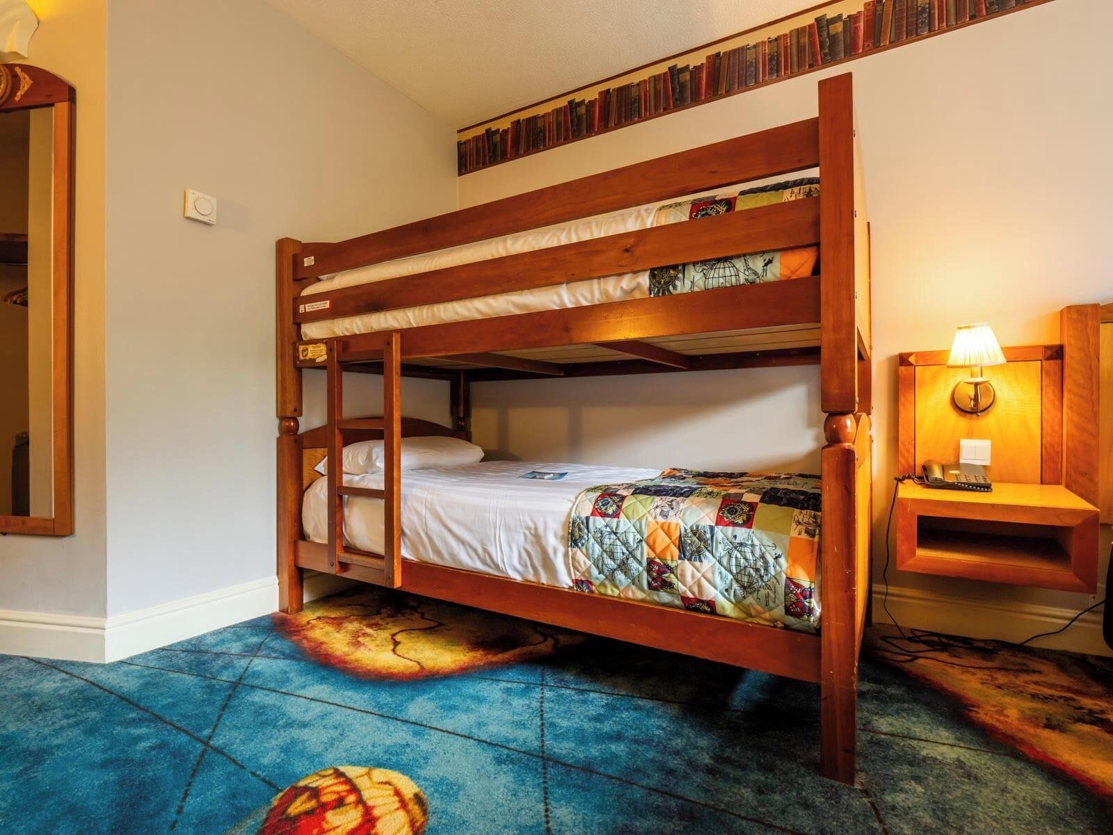 A bunk bed with a quilted bedspread, a bedside lamp, and a bookshelf with books.