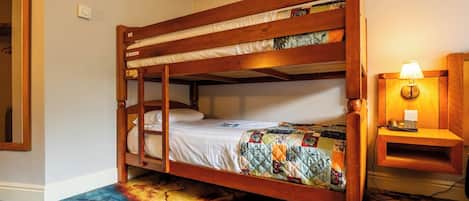 Una cama litera con cubrecama acolchado, una lámpara de noche y una estantería con libros.