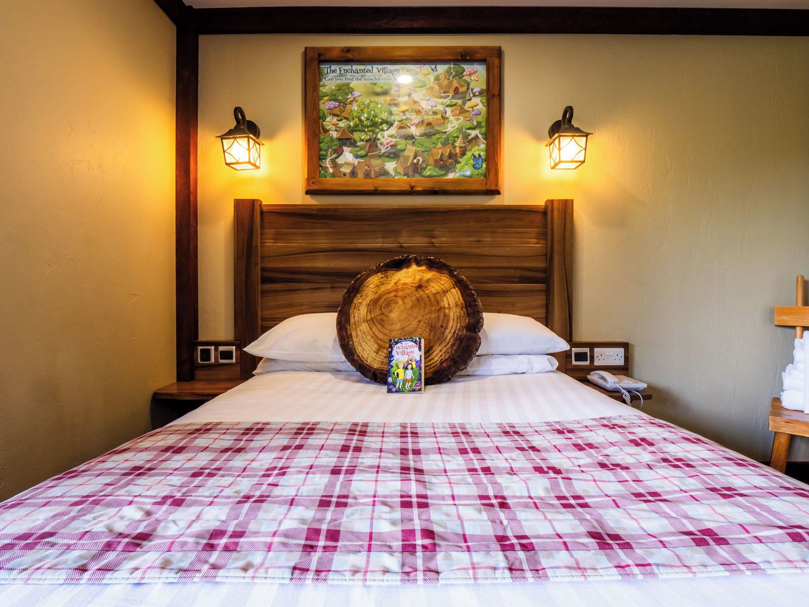 Ein Hotelzimmer mit einem großen Bett, einem Holzkopfstück, zwei Wandlampen, einem Gemälde über dem Bett und einem Nachttisch mit Telefon und Lampe.