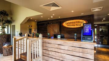 A reception desk with a wooden finish, a digital kiosk, and a sign reading 'Enchanted Village Welcome Desk.'