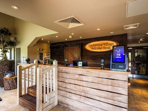 A reception desk with a wooden finish, a digital kiosk, and a sign reading 'Enchanted Village Welcome Desk.'