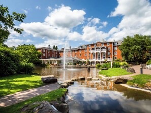 A large red brick building with a fountain in the center, surrounded by a well-maintained garden and a pond. - Alton Towers Hotel (Stoke-on-Trent)