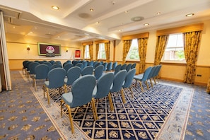A conference room with rows of chairs, a carpeted floor, and a screen displaying a logo.