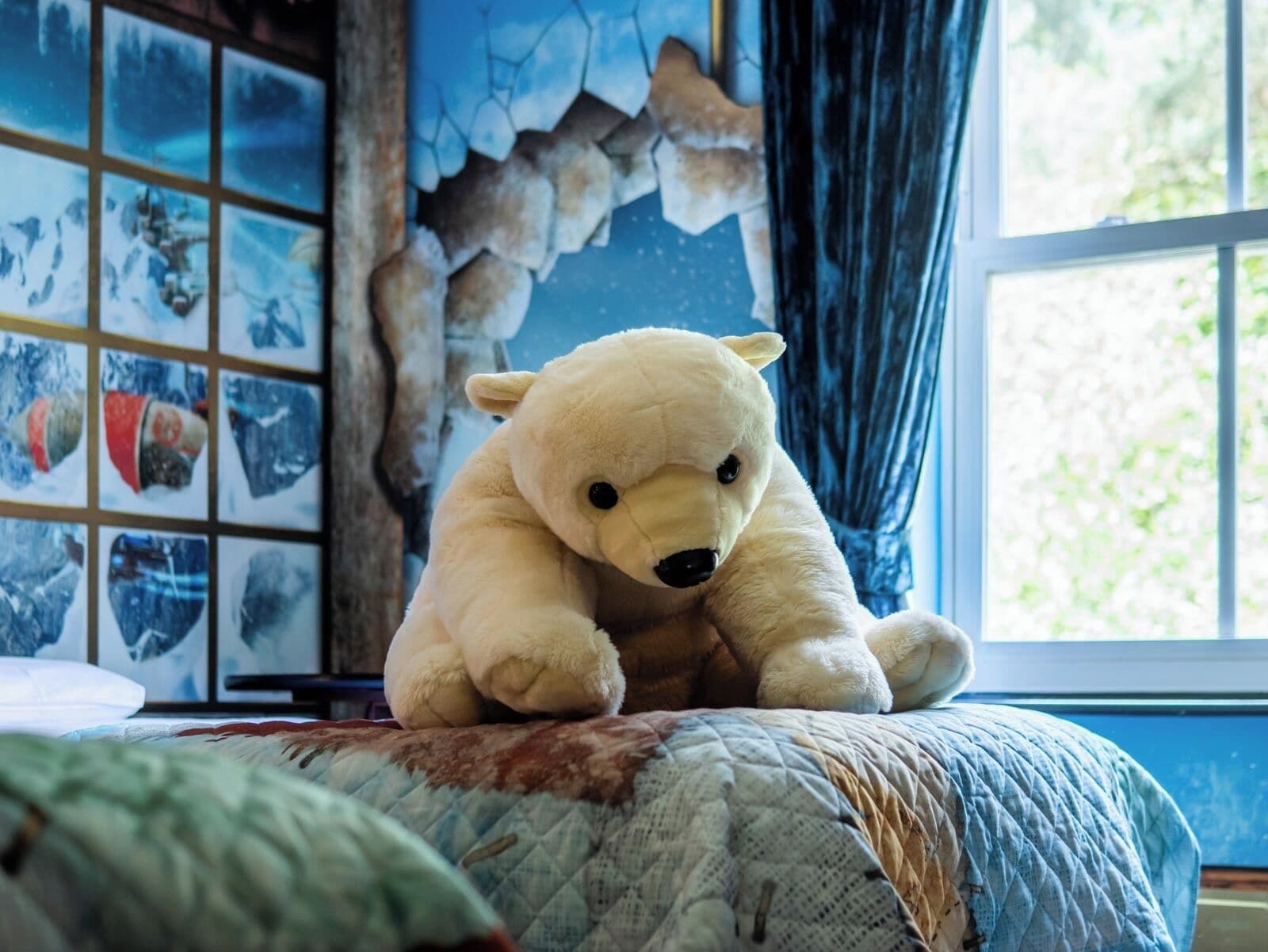 A room with a bed, a stuffed bear, a window, and a wall with pictures.