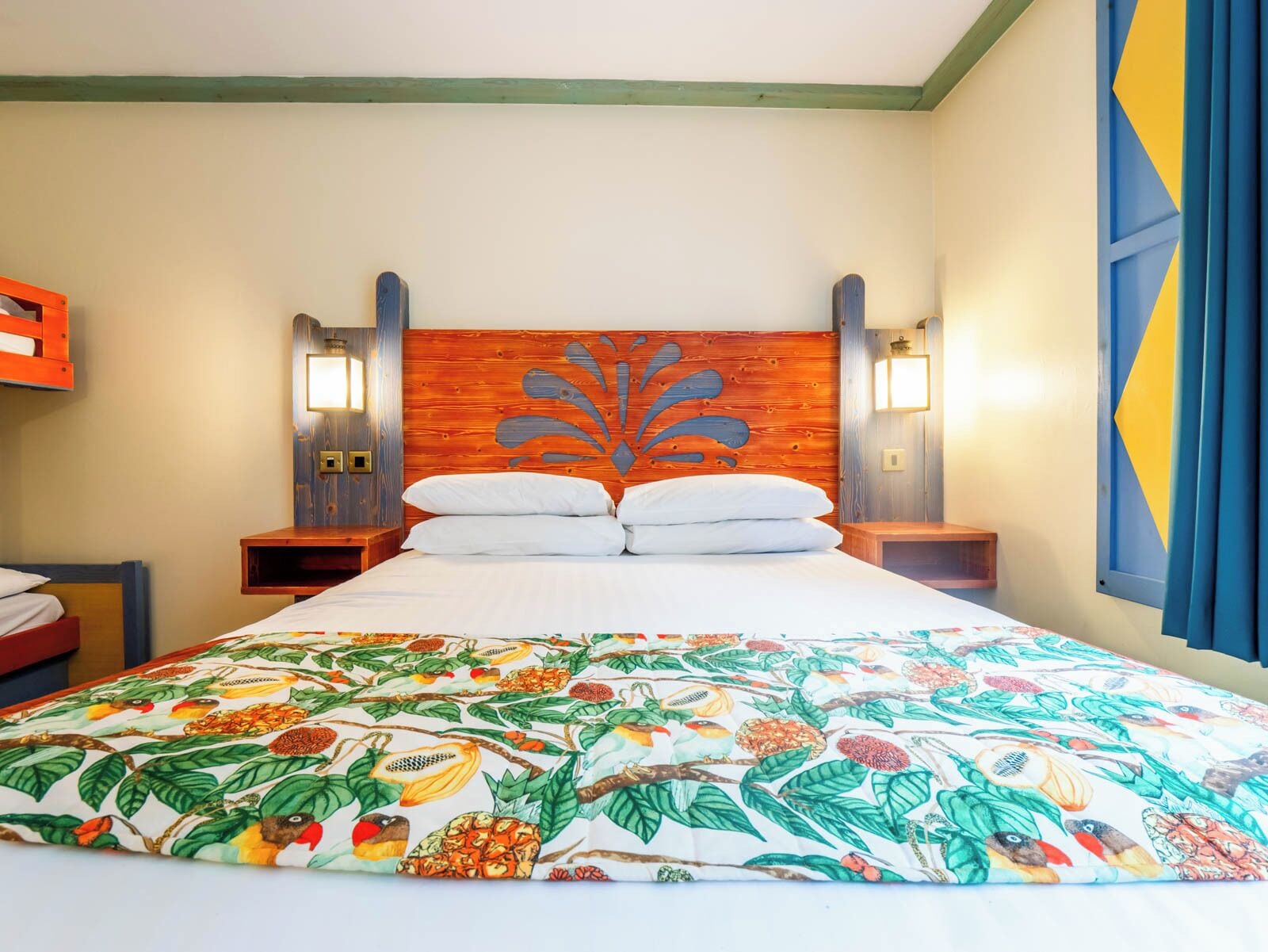 Una habitación de hotel con una cama grande, un cabecero de madera, dos mesitas de noche y una colcha colorida.