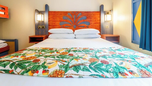 Una habitación de hotel con una cama grande, un cabecero de madera, dos mesitas de noche y una colcha colorida.