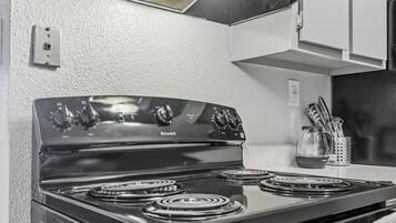 Una cocina con estufa negra, alacenas blancas y extractor.