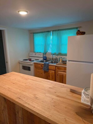 Une cuisine avec un plan de travail en bois, une cuisinière, un réfrigérateur et une fenêtre avec des rideaux.