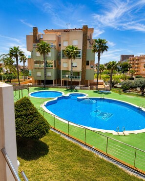 A multi-story building with a swimming pool, palm trees, and a clear sky. - Cala Flores Residence – 3-Bedroom, Pool & Terrace (Cabo de Palos)
