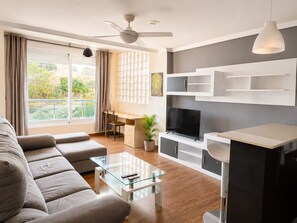 A modern living room with a sofa, a glass coffee table, a flat-screen TV, and a ceiling fan. - Cala Flores Residence – 3-Bedroom, Pool & Terrace (Cabo de Palos)