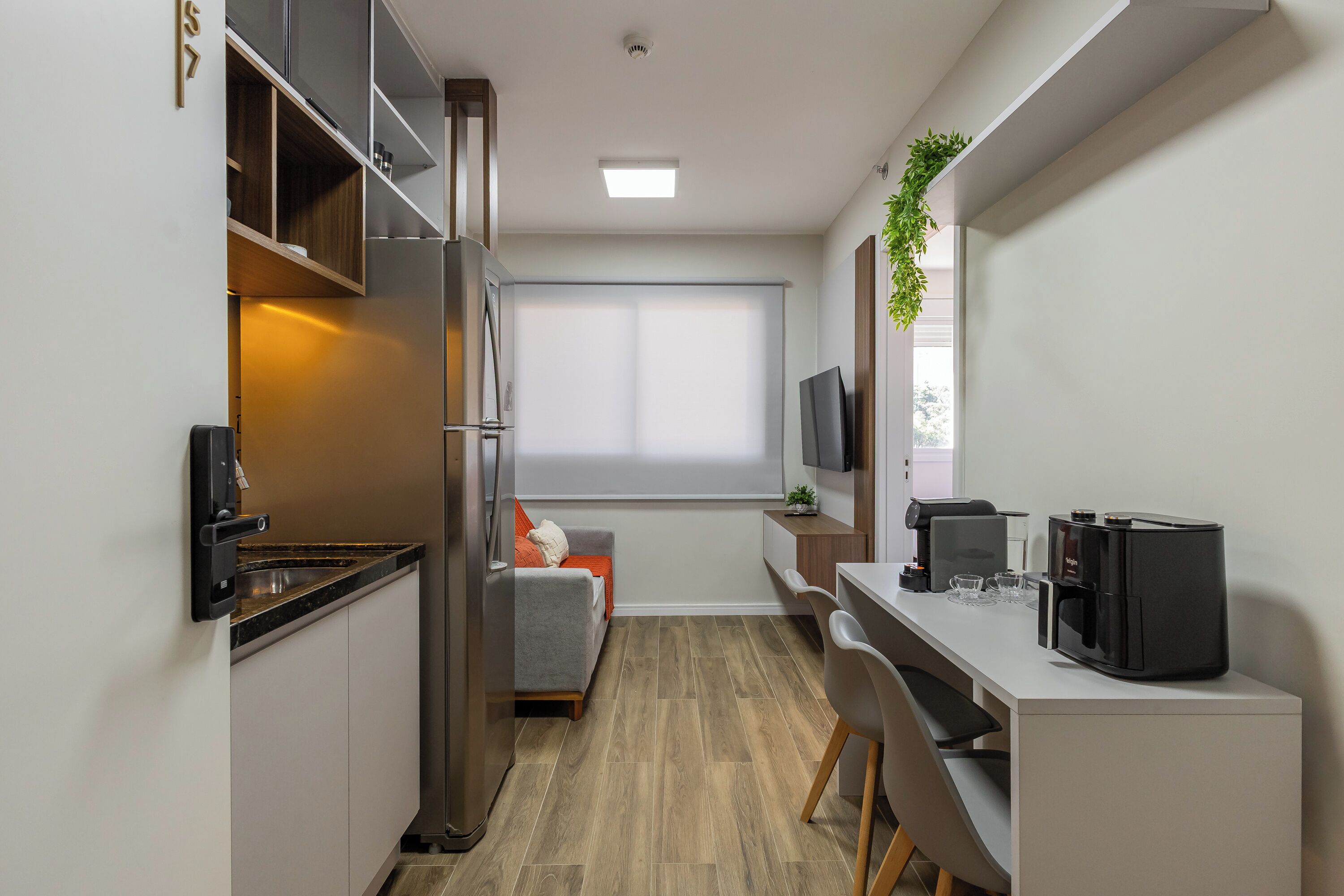 A compact kitchen with a refrigerator, a coffee machine, and a small dining area with a sofa and chairs.
