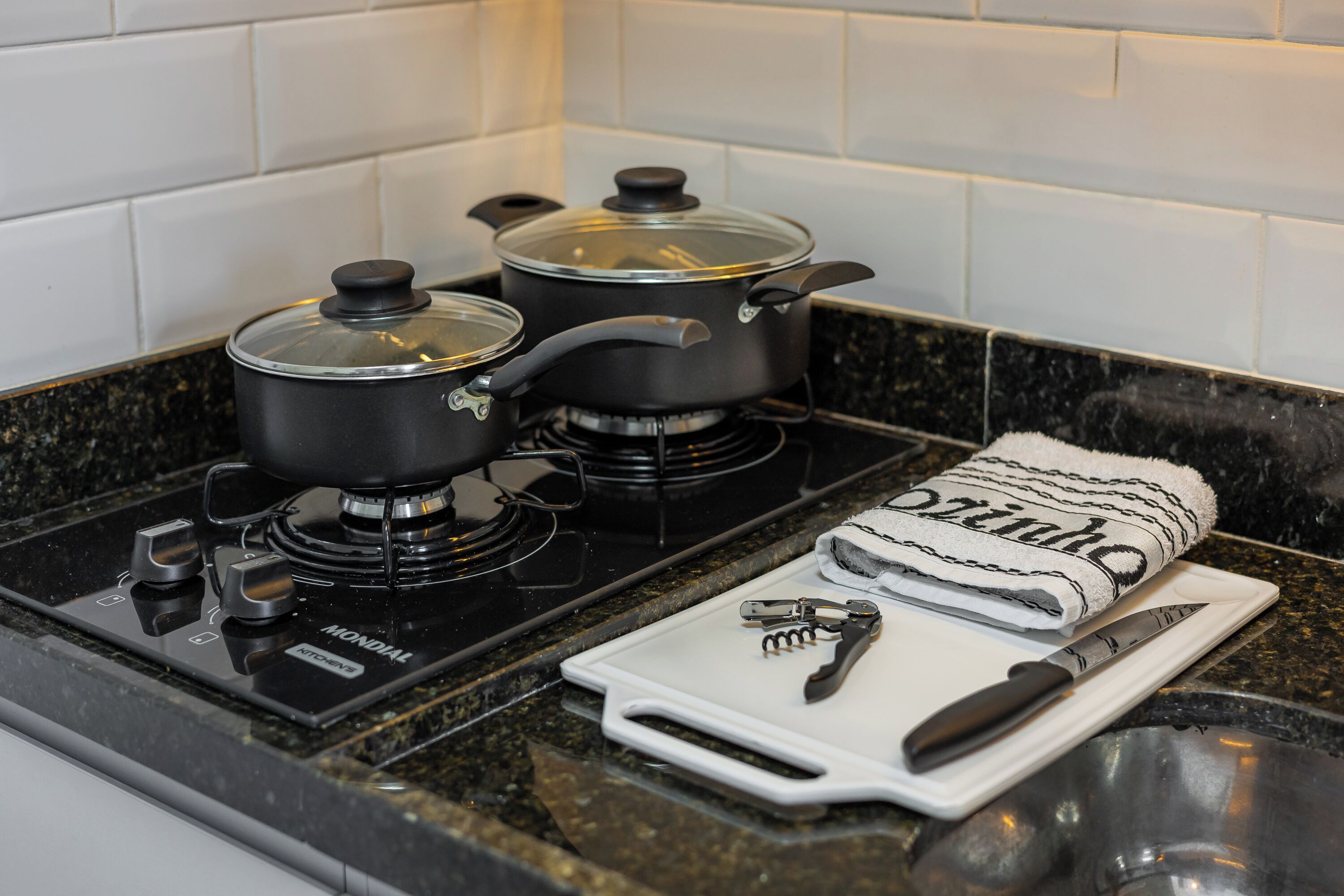 A kitchen with two pots on a stove, a cutting board with a knife and a can opener, and a towel on the counter.