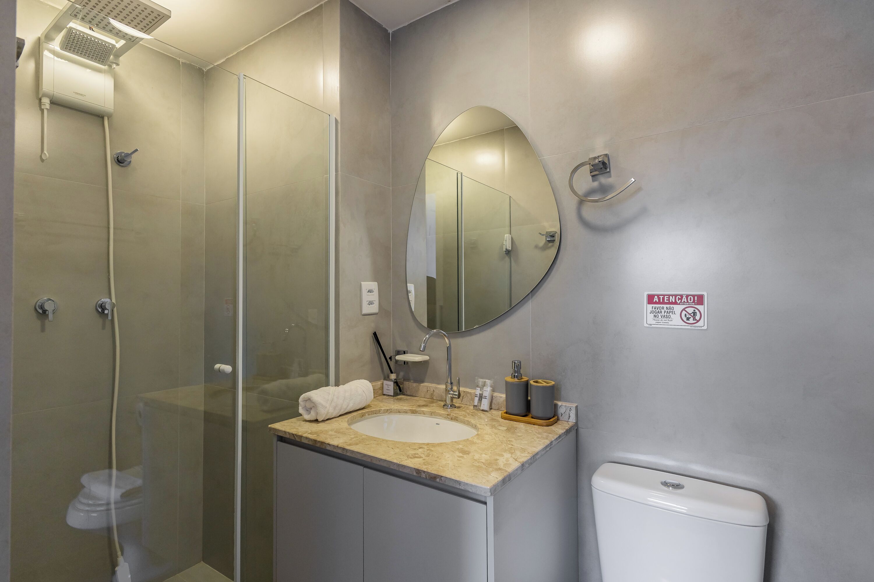 A modern bathroom with a glass-enclosed shower, a round mirror, and a toilet.