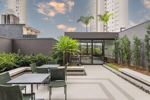 A rooftop patio with outdoor seating, a glass door entrance, and a view of tall buildings. - StayHome Chácara Klabin - AC & Gym (São Paulo)