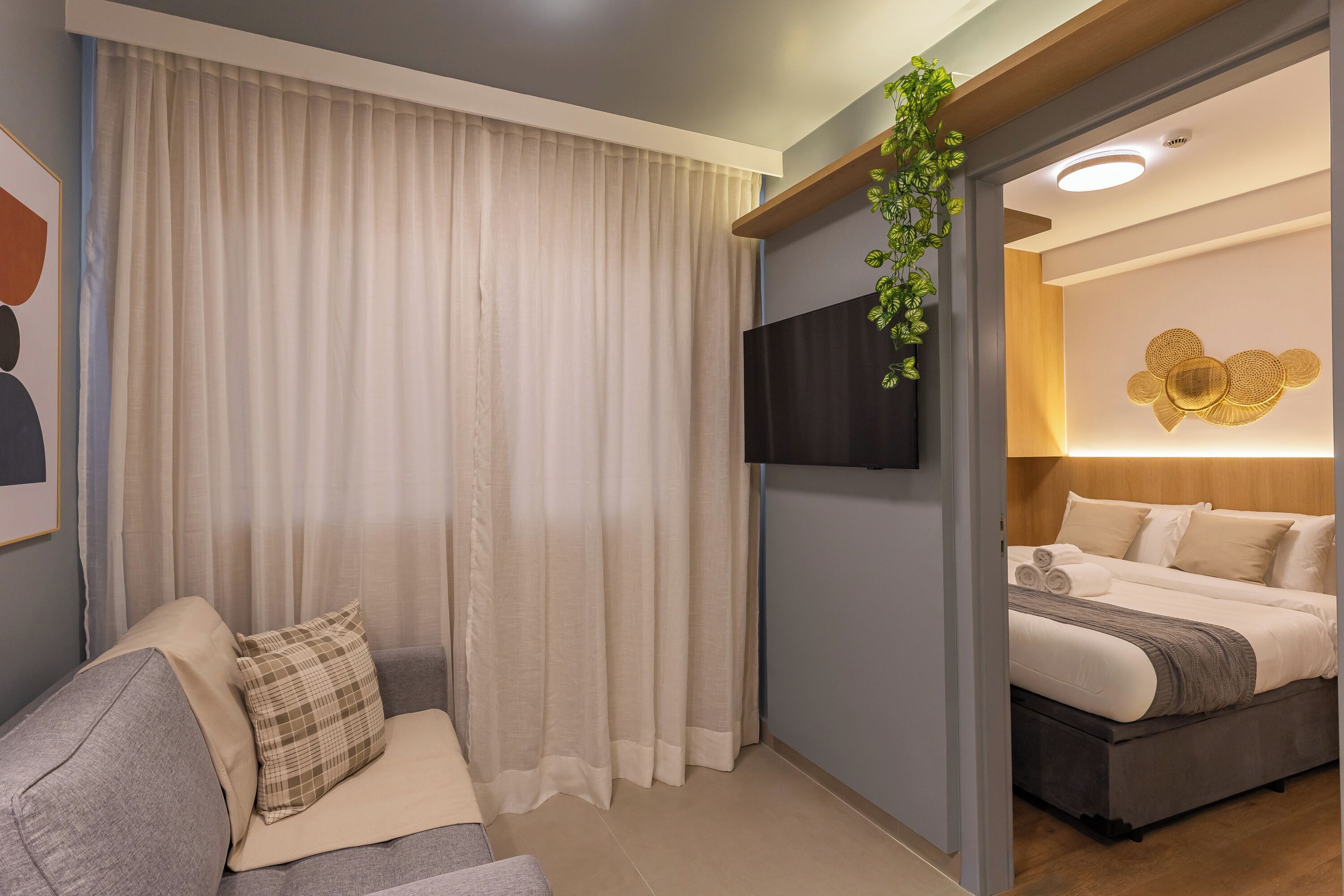 Ein modernes Hotelzimmer mit einem Bett, einer Couch, einem Fernseher und einer Wandpflanze.