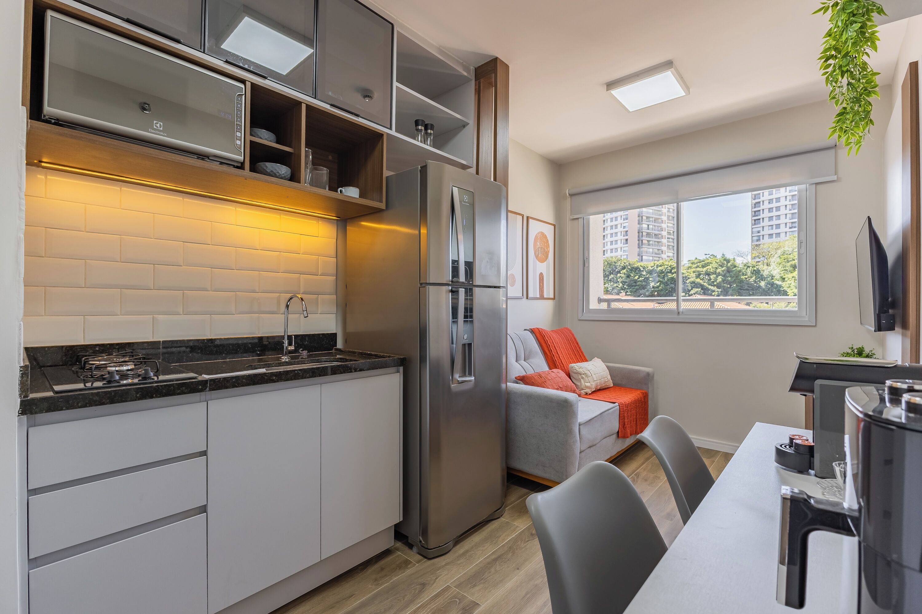 A modern kitchen with a built-in oven, stainless steel refrigerator, and a dining area with a grey sofa and a table.