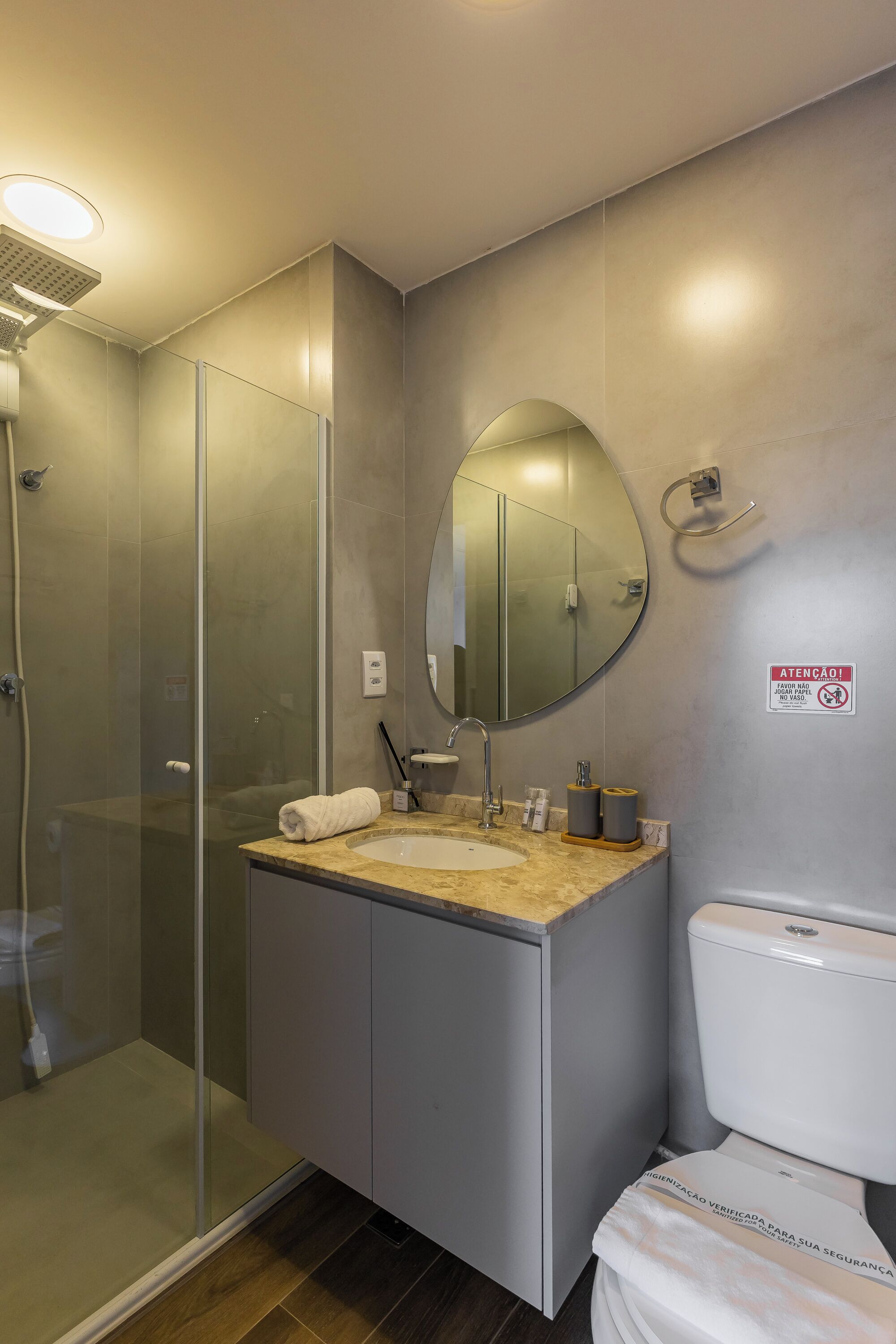 Um banheiro moderno com chuveiro em box de vidro, pia com bancada de mármore e vaso sanitário.