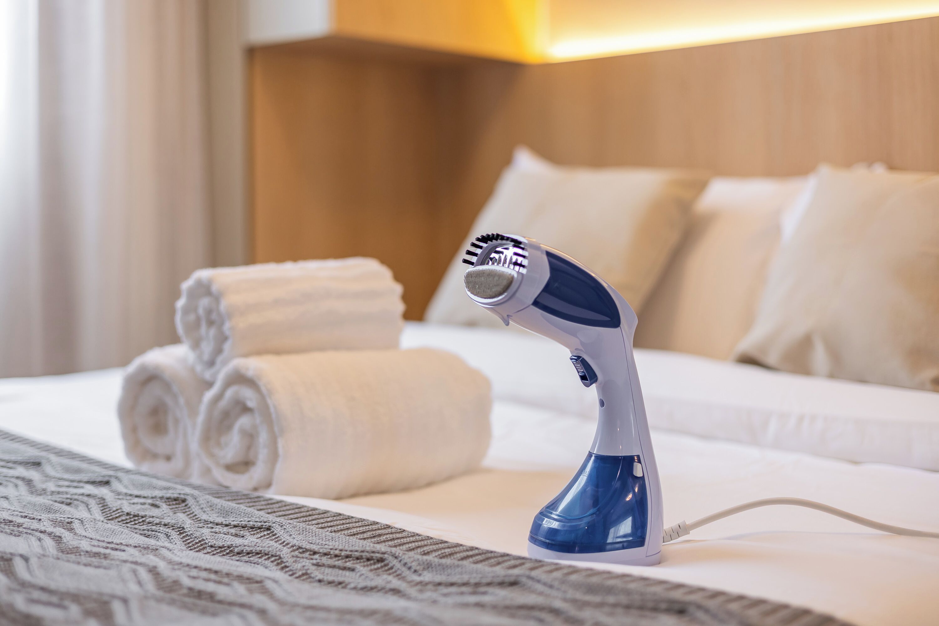 A hotel room with a bed, rolled towels, and a hairdryer on the bed.