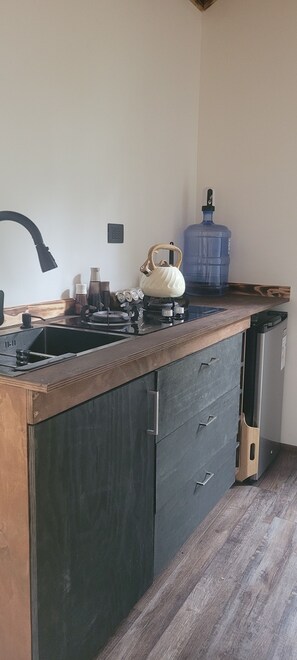 A kitchen with a sink, a kettle, a water dispenser, and a cabinet.