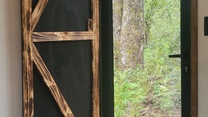 Een kamer met een houten deur die uitkomt op een buitenruimte met uitzicht op bomen en een houten terras.