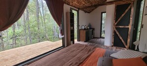A bedroom with a large window, a bed, a wooden floor, and a view of the forest. - Shinrin Lodge | River, forest, clay tub, breakfast, transportation. All-inclusive (Huililco)