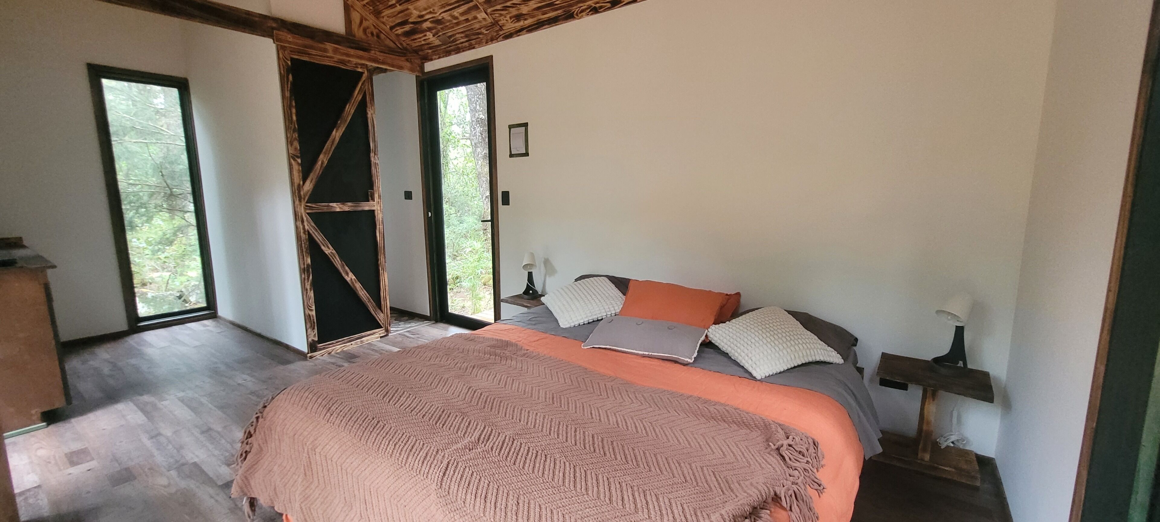 Un dormitorio con cama, almohadas, una mesita de noche y vistas a través de una puerta abierta.