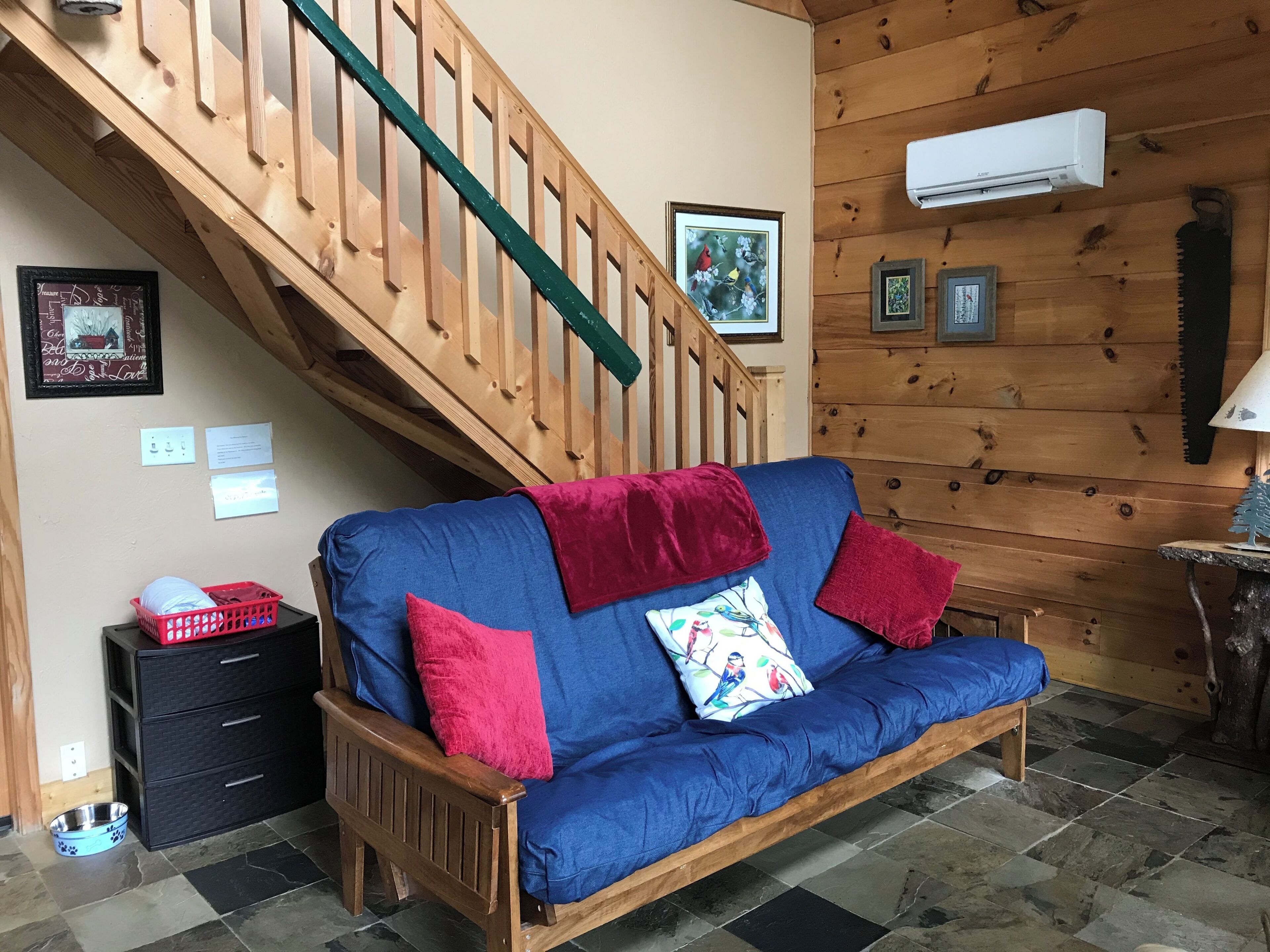 A wooden staircase, a blue sofa with red cushions, a framed picture, and a small table with a lamp.