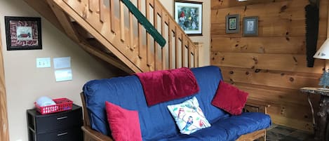 Una escalera de madera, un sofá azul con cojines rojos, un cuadro enmarcado y una mesita con una lámpara.