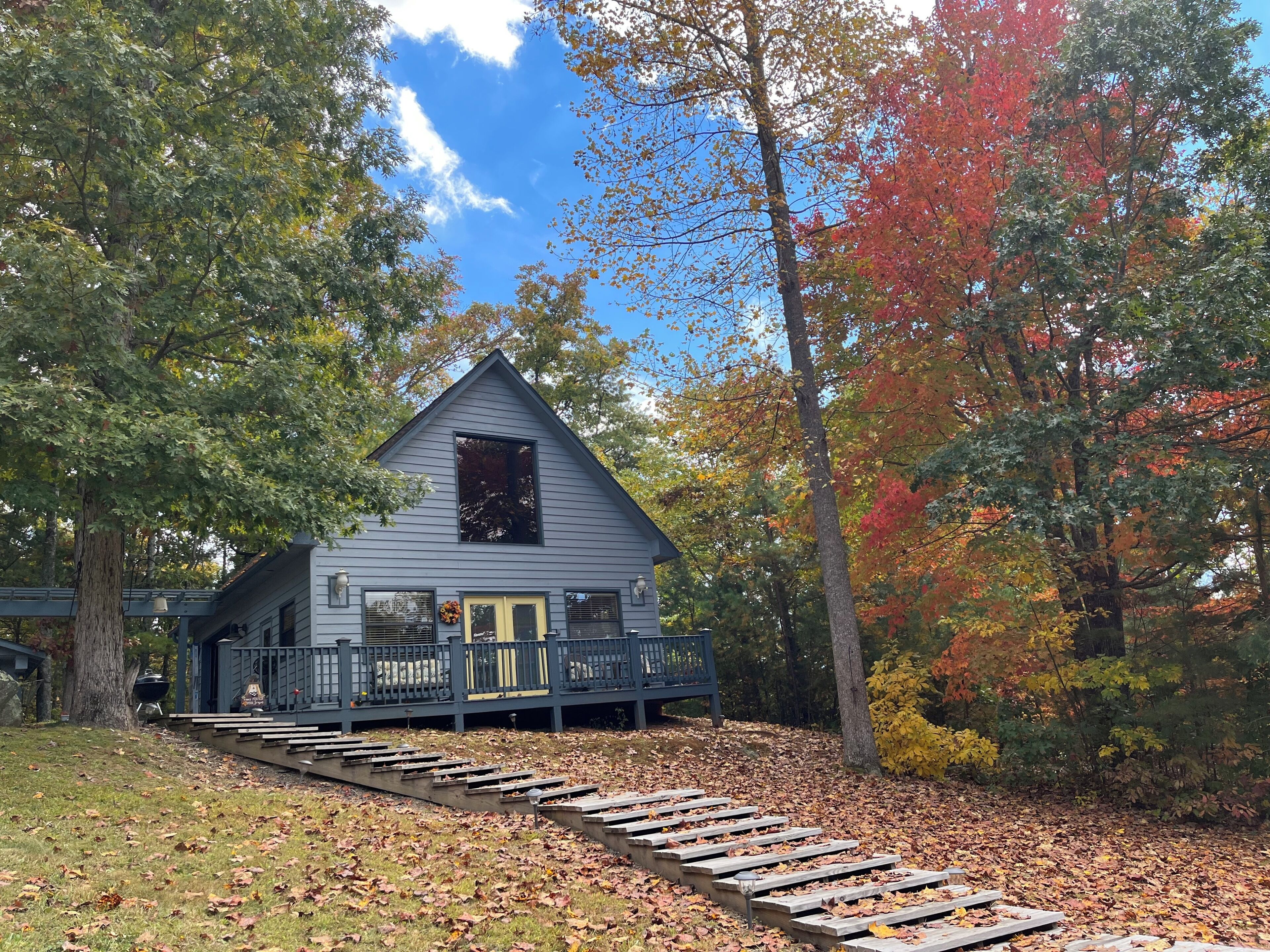 Eine Holzhütte mit Veranda und Stufen, umgeben von Bäumen und herabgefallenen Blättern.