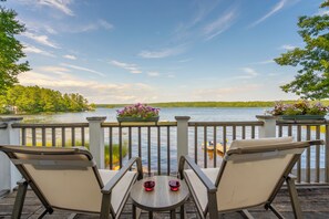 Una terraza con dos sillas y una mesa, con vista a un lago y una orilla boscosa.