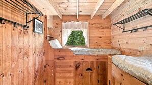 Interior de cabaña acogedora con literas, una ventana pequeña que da a la vegetación y un cuadro en la pared.