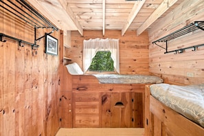 A compact cabin interior with a bunk bed, a small window with a view of greenery, and a framed picture on the wall.
