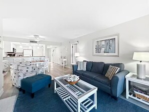 Ein modernes Wohnzimmer mit einem blauen Sofa, einem Glastisch und einem Essbereich mit weißer Möbel.