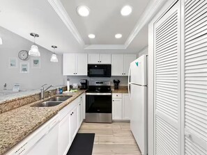 Eine moderne Küche mit weißen Schränken, Granit-Arbeitsplatten, Edelstahlgeräten und Pendelleuchten.